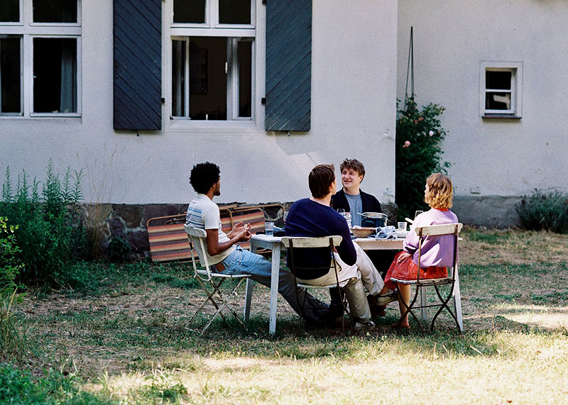 El cielo rojo - fotograma de la película se ve a 3 chicos y una chica comiendo en un jardín