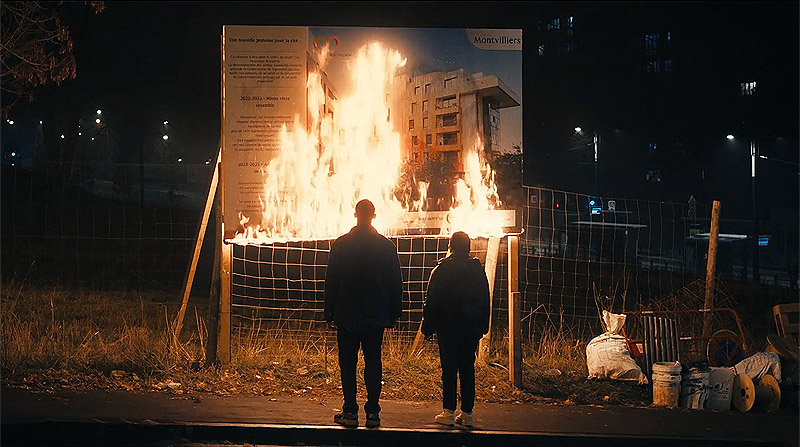 Los indeseables - imagen de la película se ve a 2 personas mirando un cartel ardiendo