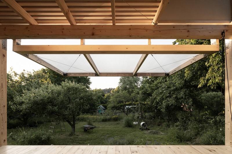 byro-architekti-garden-pavilion: pabellón de madera oscura de perfil con fachada abierta y vista al jardín