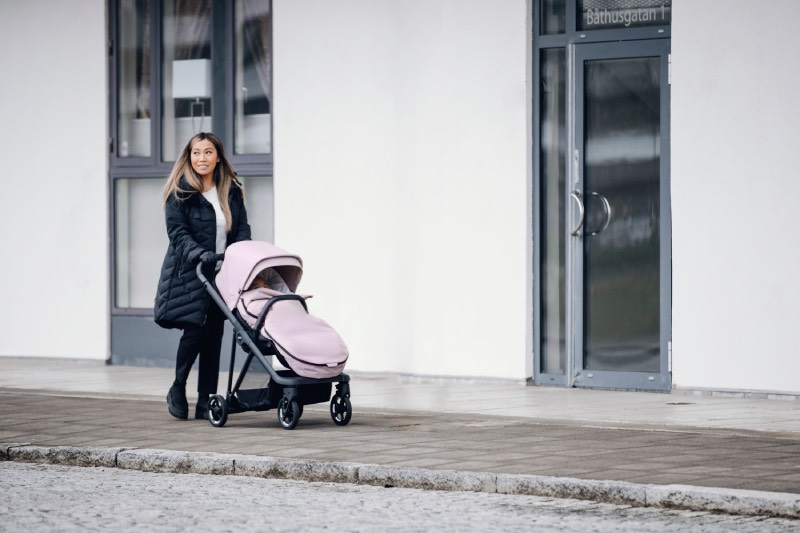 cochecitos urbanos: una mujer pasea con su bebé en un carrito rosa de Thule
