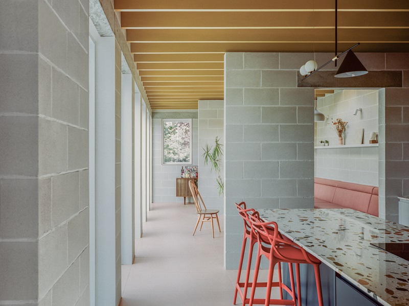 Triangle-House-Artefact: comedor con sofá rosa, isla de terrazo y techo dorado