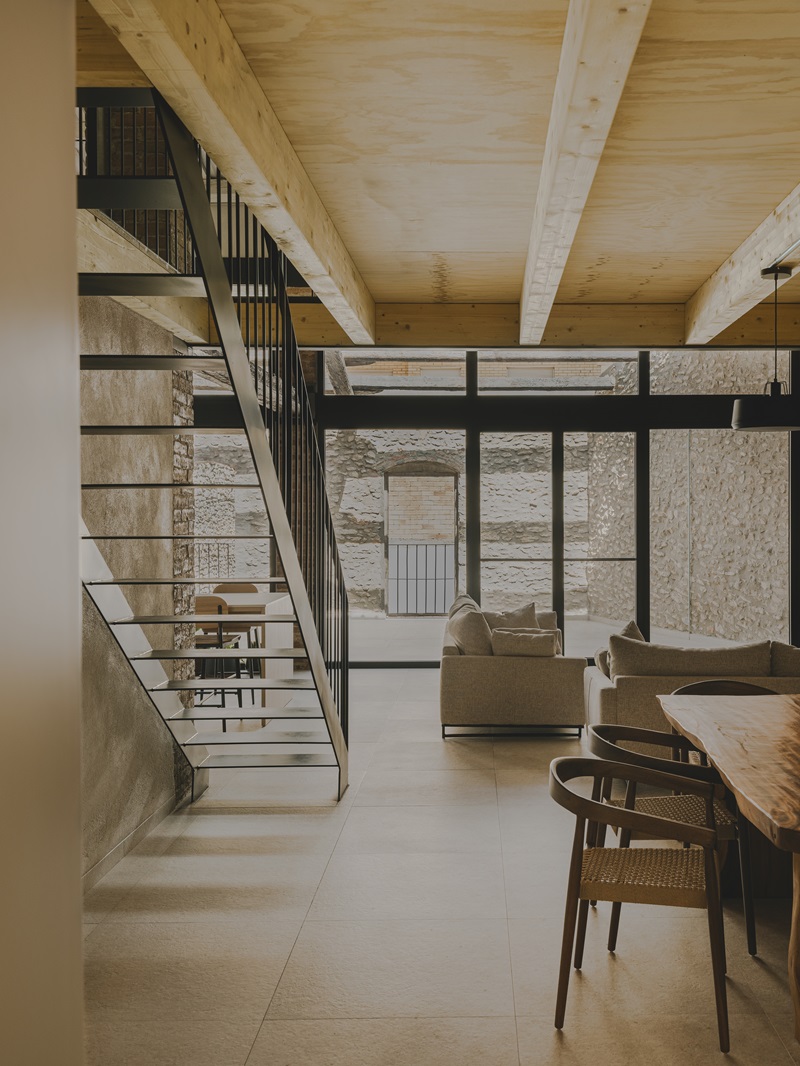 VVAA-studio- Migdia-II: mesa de comedor y techo de viguetas de madera frente a ventanal del salón y escalera metálica