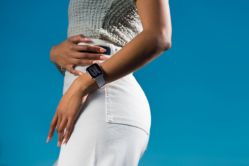 Amazfit Active: el torso de una mujer queporta el reloj inteligente Amazfit Active en su muñeca. Lleva ropa casual y la foto está tomada en un estudio fotográfico.