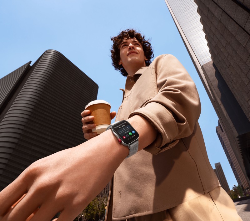 Huawei Summer Wave: un chico joven porta un café entre edificios altos de la ciudad y en la otra muñeca lleva el WATCH FIT 3 Sport Edition