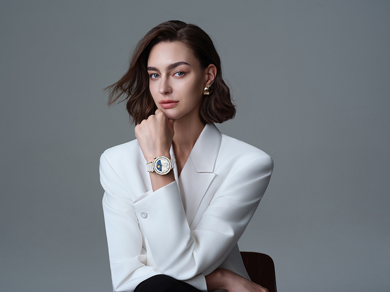 Huawei Watch GT 5 Pro: una mujer con melena corta viste elegante con una americana blanca y un reloj inteligente Huawei Watch GT 5 Pro de cerámica en blanco. La foto, de plano medio, está tomada en un estudio profesional con fondo gris.