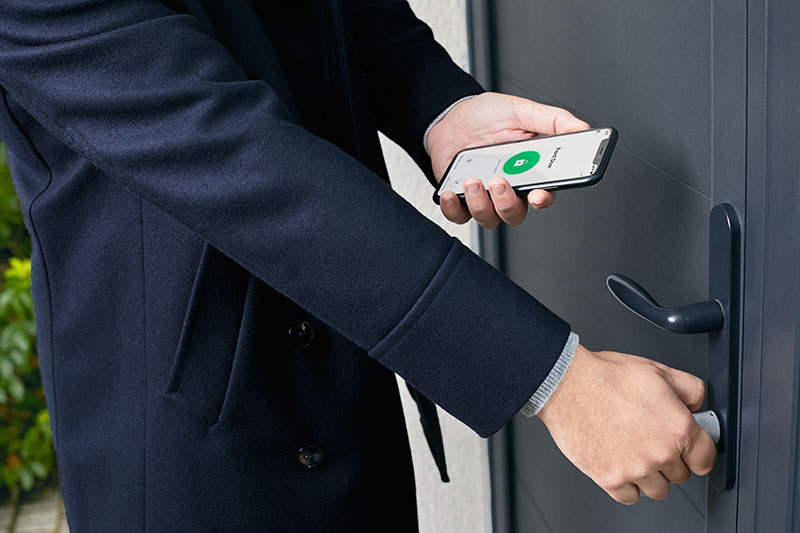 cerradura inteligente: un hombre con traje, abre la puerta de una casa con jardín desde su smartphone