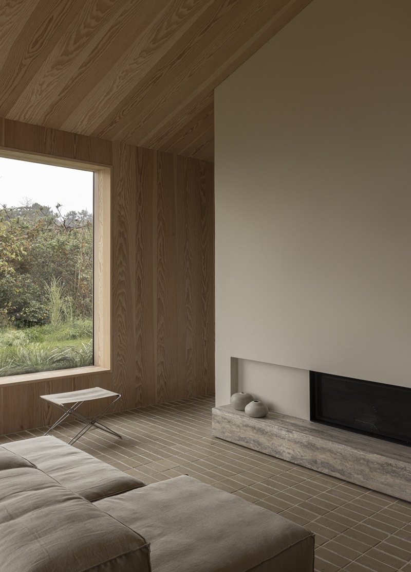 Norm-Architects-Heatherhill-Beach-House: salón con chimenea, paredes de madera y suelo de ladrillo