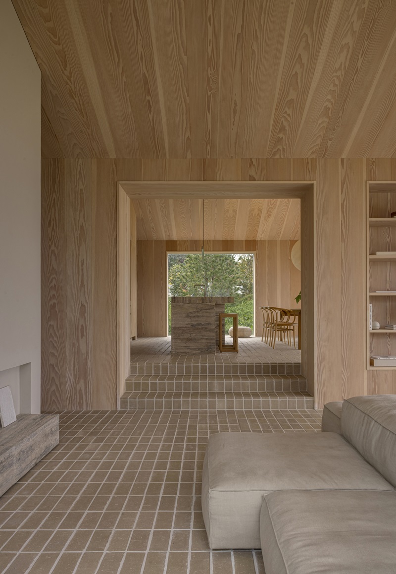 Norm-Architects-Heatherhill-Beach-House: cocina con isla de travertino, paredes de madera y suelo de ladrillo