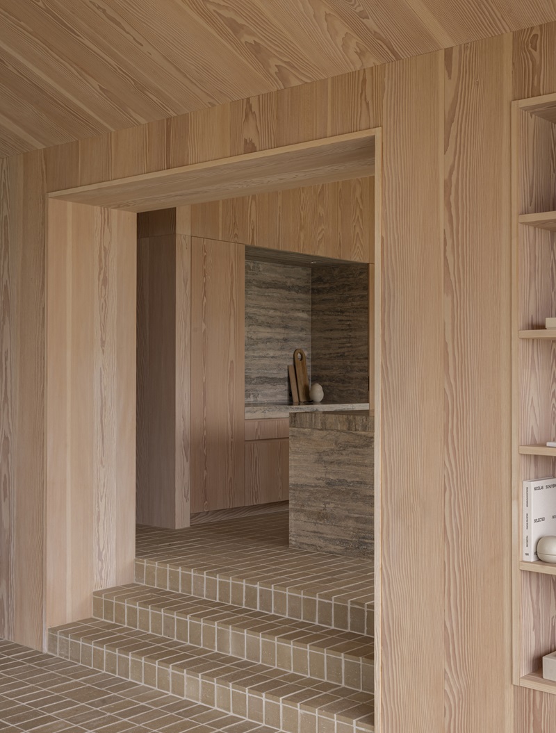 Norm-Architects-Heatherhill-Beach-House: cocina con isla de travertino y muebles de madera