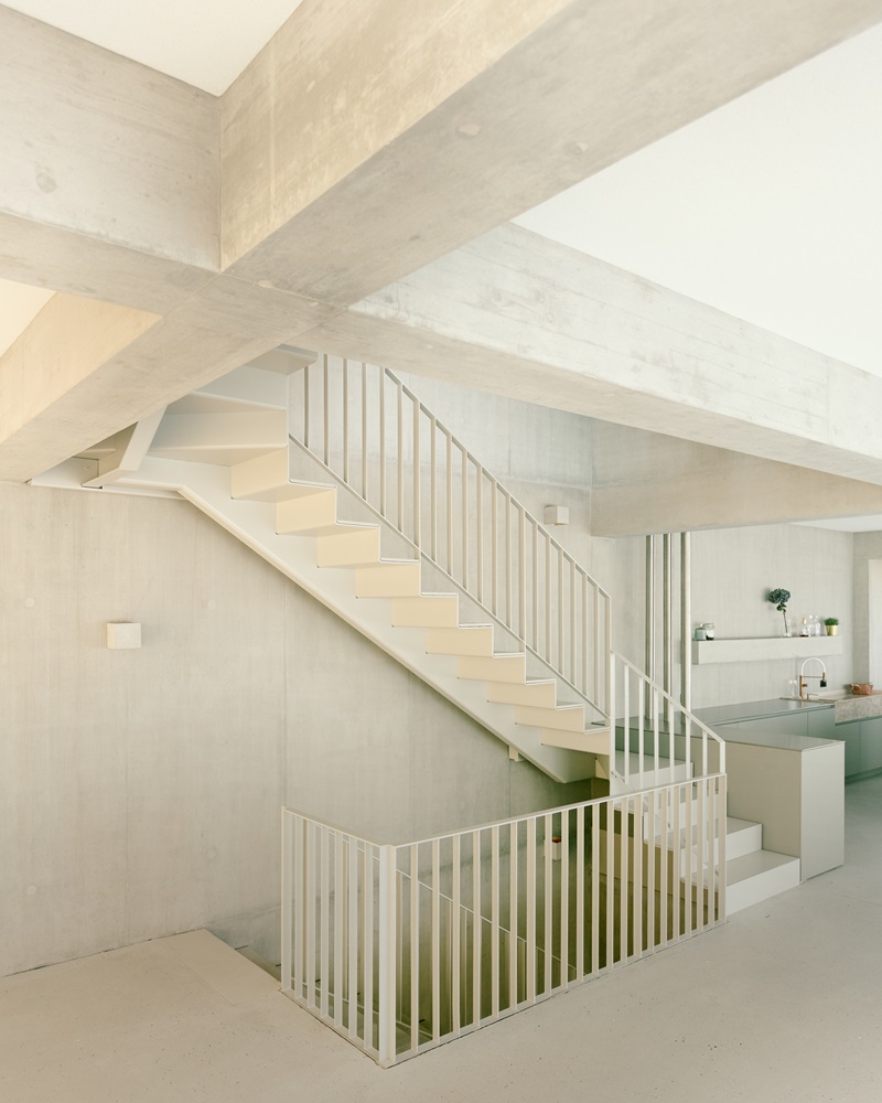 Oberwil-House-Caesar-Zumthor: sala de estar con vigas y pilares de hormigón y escalera metálica blanca