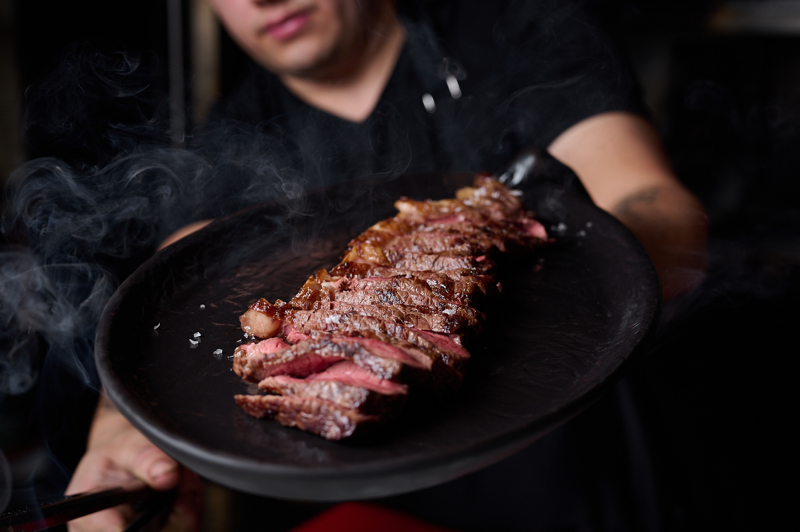 Al Fuego Madrid: carne cocinada, fileteada y dispuesta en una bandeja negra.