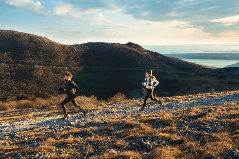 Fēnix 8: un hombre y una mujer corren por un sendero de montaña en un día soleado