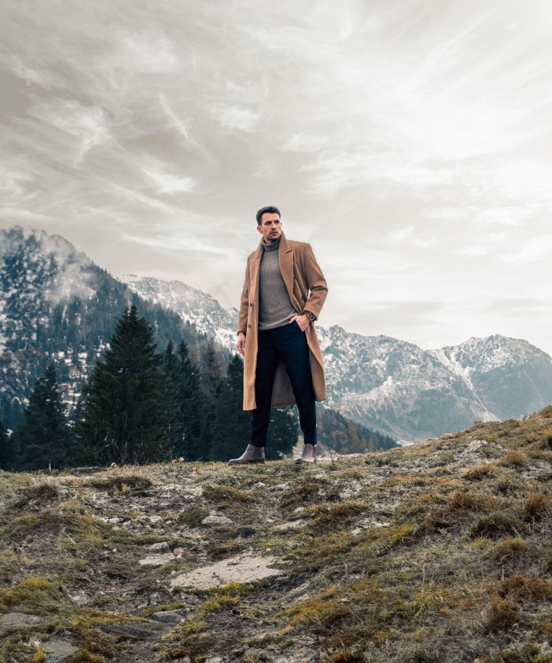 Fēnix 8: un hombre elegante posa con su reloj inteligente de Garmin para una foto de plano general en la montaña en un día nublado