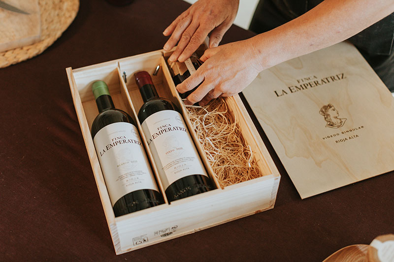 Una caja de madera elegante que contiene dos botellas de vino de Finca La Emperatriz, una de vino tinto y otra de vino blanco, cuidadosamente dispuestas sobre un lecho de paja natural.