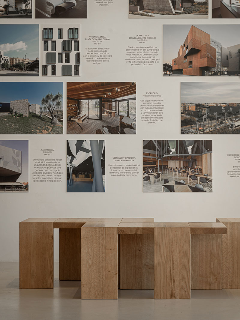 Exposicion-Camen-Pinos-Minim: banco de madera frente a fotografías de proyectos