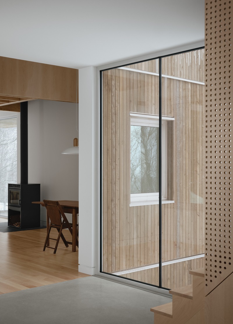 Julia-Manaças-Architecte-House-MN: sala de estar con suelo de madera y mesa de comedor y estufa de leña junto al cristal de la pasarela