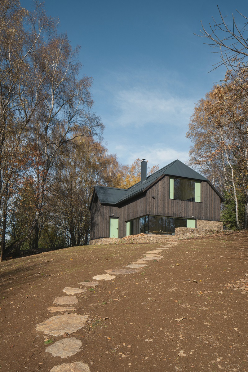 marketa-cajthamlova-cottage-in-sumava: casa de madera en la naturaleza con tejado inclinado y camino de piedras