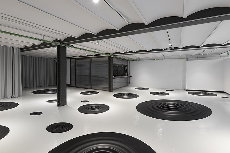 Fluctus Lacus, Carmen Ortíz - instalación artística de piezas circulares de caucho negro con forma de ondulaciones circulares colocadas en el suelo de una galería de arte