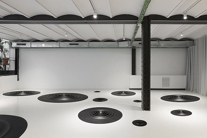 Fluctus Lacus, Carmen Ortíz - instalación artística de piezas circulares de caucho negro con forma de ondulaciones circulares colocadas en el suelo de una galería de arte