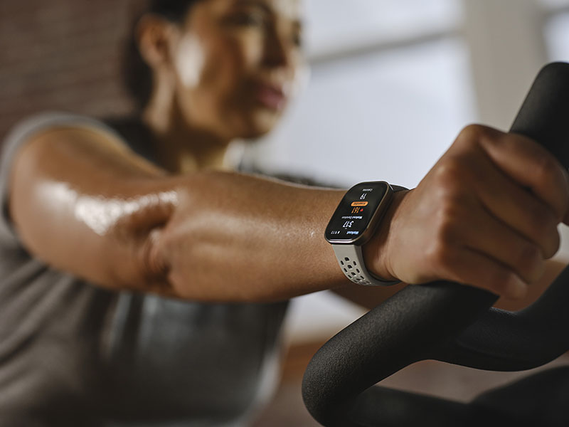 Amazfit Bip 6: foto detalle de la mano derecha de una mujer que entrena sobre una bicicleta estática y lleva puesto el reloj Amazfit Bip 6.