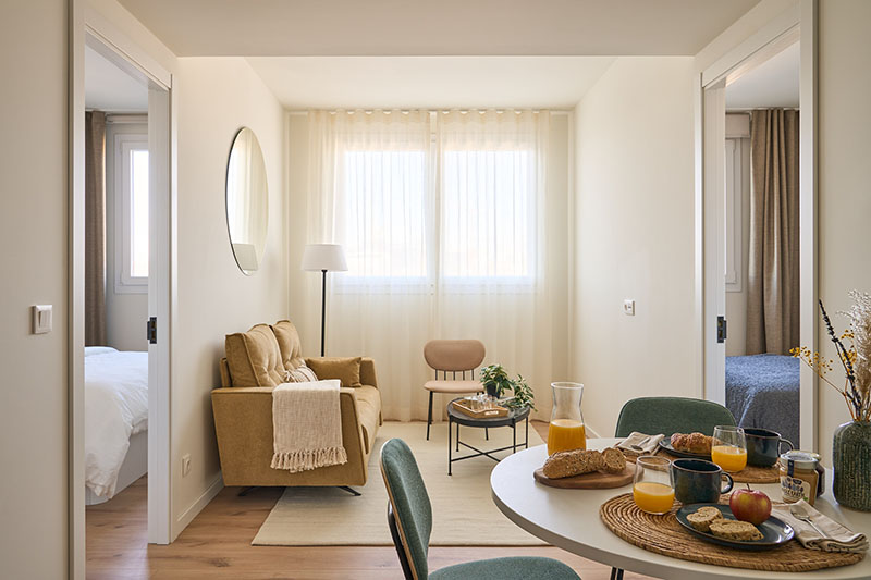 Be Casa Alcobendas: salon comedor acogedor de un apartamento flexible de Be Casa Alcobendas con dos dormitorios. Es por la mañana, entra luz natural y sobre la mesa hay un desayuno para dos.