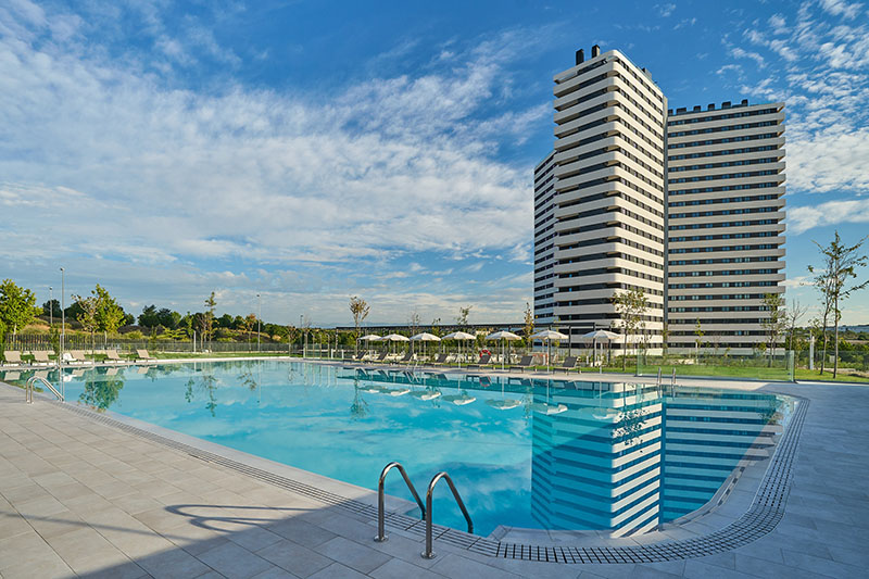 Be Casa Alcobendas: zona de la gran piscina exterior de Be Casa Alcobendas con sombrillas y hamacas en un día soleado.