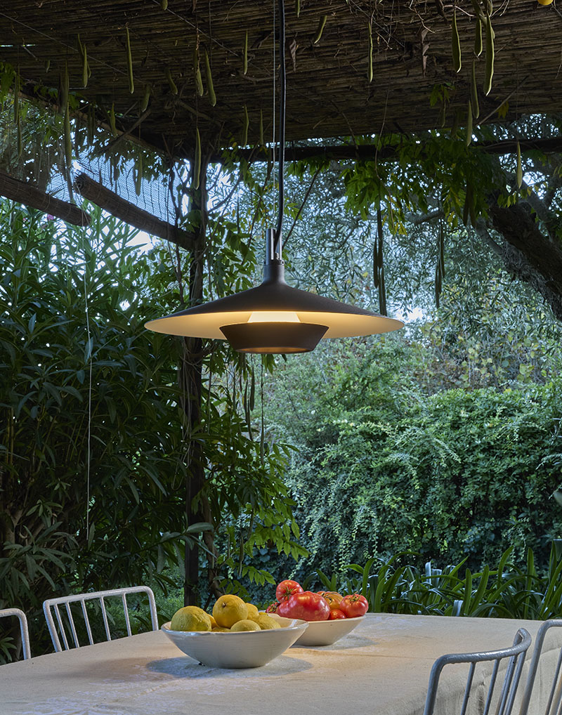 Bajo una pérgola cubierta de vegetación, un fanal de Bover en suspensión ilumina una mesa