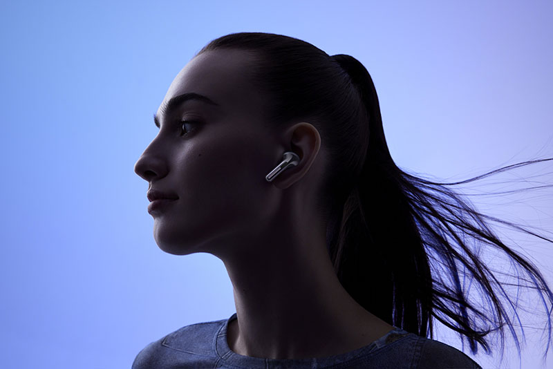 Buds Pro 3: foto retrato de una mujer que lleva los auriculares inalámbricos OnePlus Buds Pro 3 sobre fondo azul degradado.