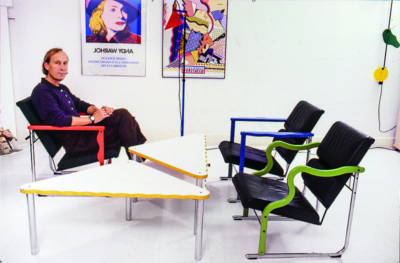 Hem: Yrjö Kukkapuro sentado en una de sus Experiment Chair en los años 80, rodeado de versiones en distintos colores y una mesa triangular de estética postmoderna