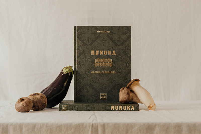 Nunuka. Cocina georgiana, un libro que recoge las recetas de cocina georgiana, sobre un mantel con berenjenas, puerros, setas y patatas