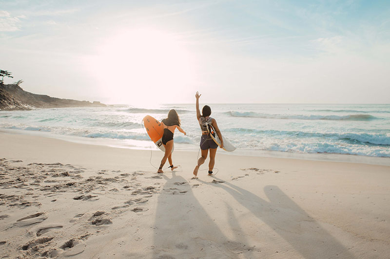 Dos personas con tablas de surf caminando por la playa cercana a Wecamp Reserva Alecrim