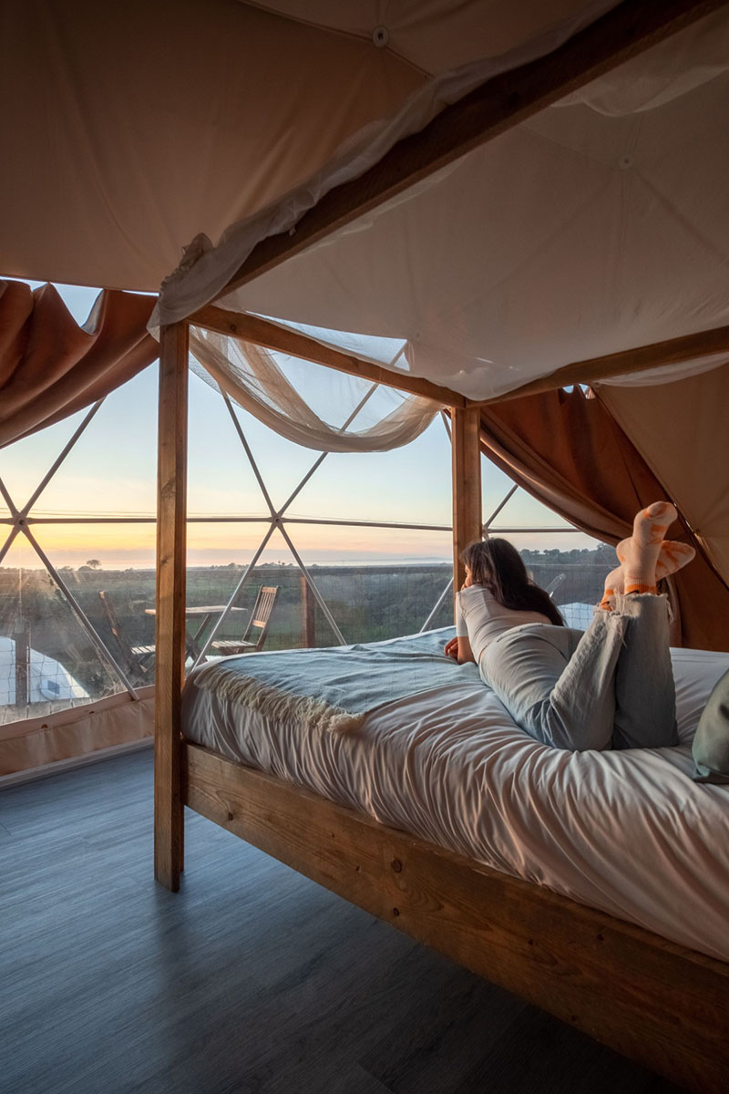 Interior de un domo en Wecamp Reserva Alecrim, con cama orientada hacia un ventanal con vistas al paisaje