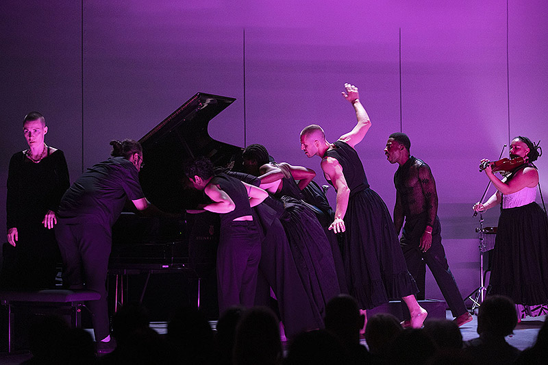 Actores de performance sobre un piano y con luz violeta