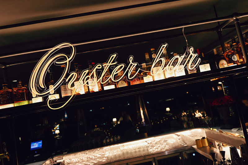 Cartel de neón con el nombre "Oyster Bar" sobre la barra del Oyster Bar del Club Financiero Génova