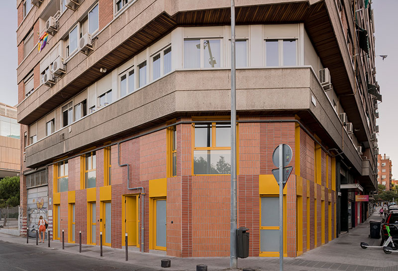 Ooiio Arquitectura: fachada de ladrillo y carpintería amarilla que marca el acceso a los apartamentos en Carabanchel