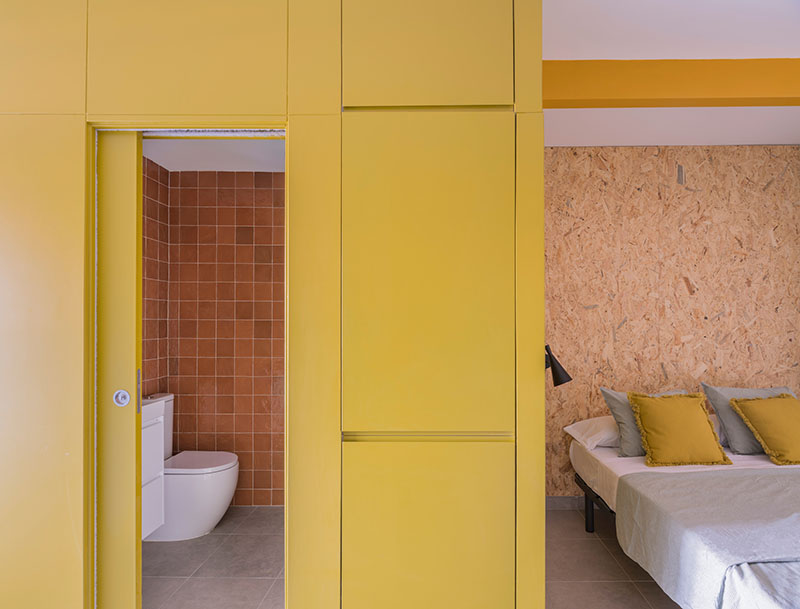 Ooiio Arquitectura: dormitorio con armarios y puerta corredera amarillos, y paredes de tablero OSB perteneciente a uno de los apartamentos en Carabanchel