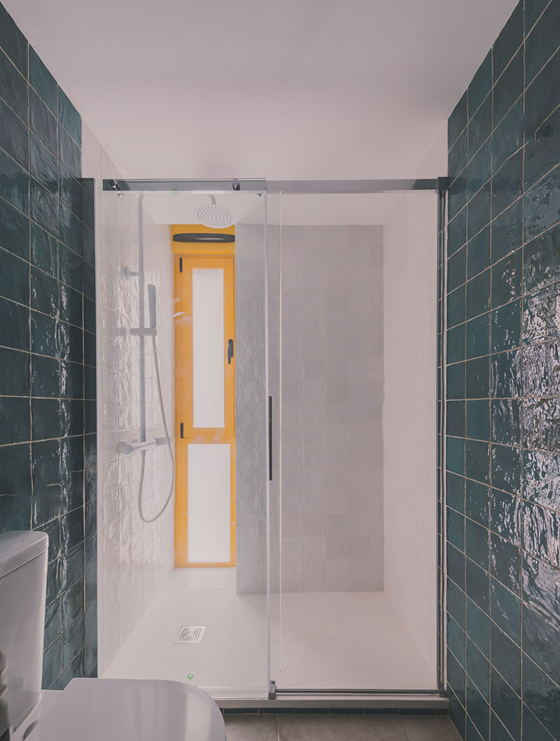 Ooiio Arquitectura: baño con azulejos verdes y blancos, y ventana amarilla que aporta luz natural perteneciente a uno de los apartamentos en Carabanchel