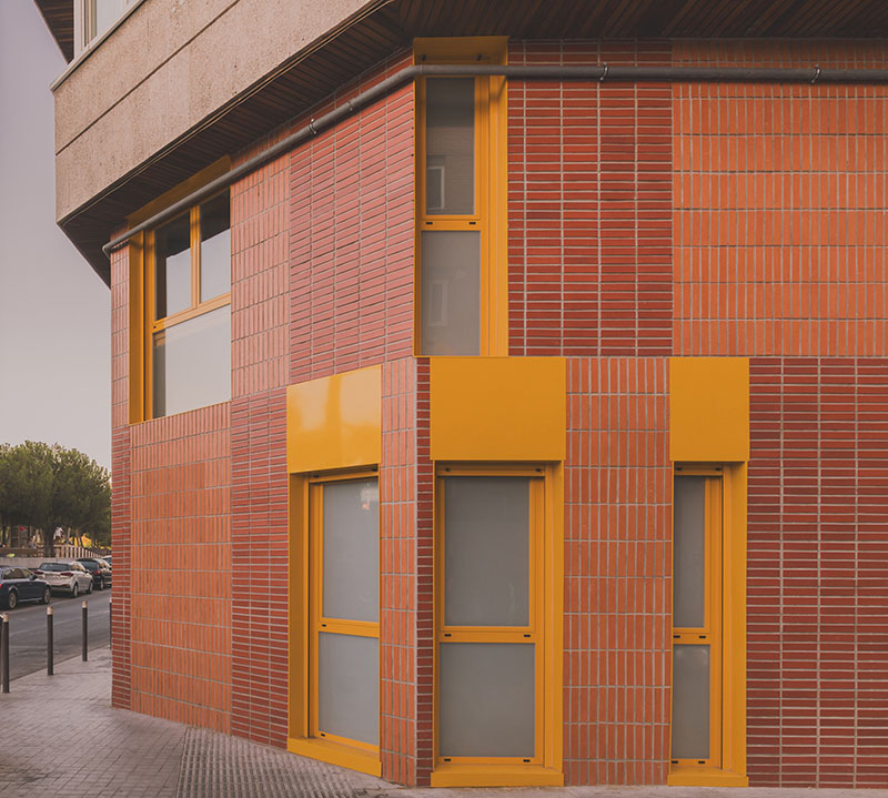 Ooiio Arquitectura: fachada de ladrillo y carpintería amarilla que marca el acceso a los apartamentos en Carabanchel