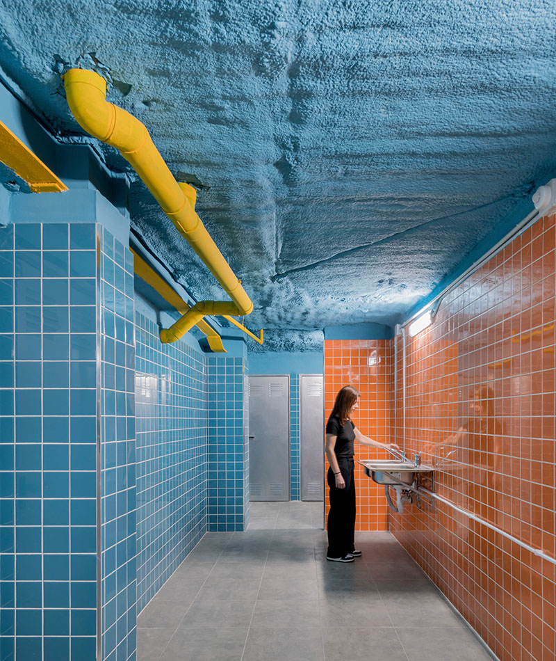 Ooiio Arquitectura: zona común con revestimiento cerámico azul y naranja, y tuberías amarillas en el techo de los apartamentos en Carabanchel