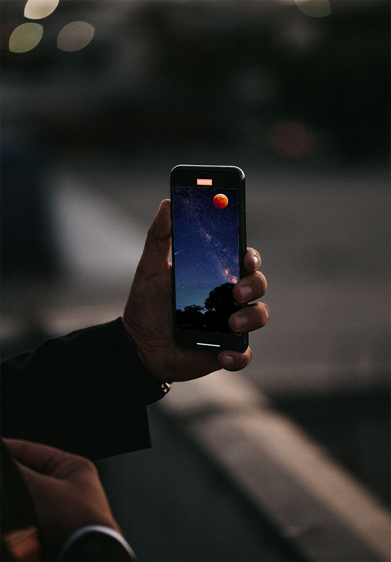 Vivo: una mano sosteniendo un teléfono móvil, que en la pantalla refleja una espectacular fotografía del eclipse lunar junto a la Vía Láctea y una estrella fugaz